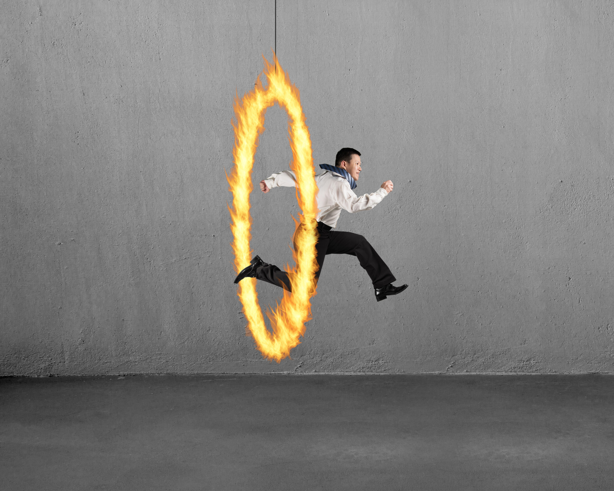 Man,jumping,through,fire,hoop,with,concrete,wall,background